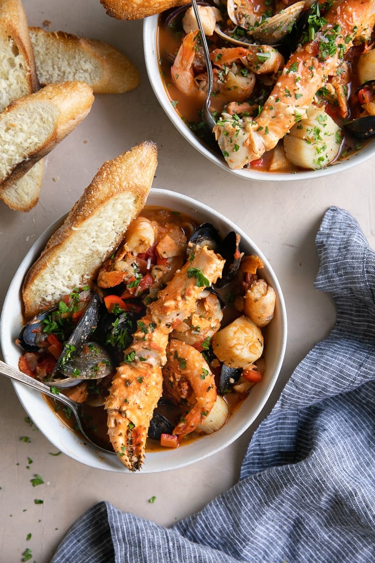 A bowl Cioppino seafood stew filled with shrimp, scallops, crab legs, fish, clams, and mussels and served with slices of bread.