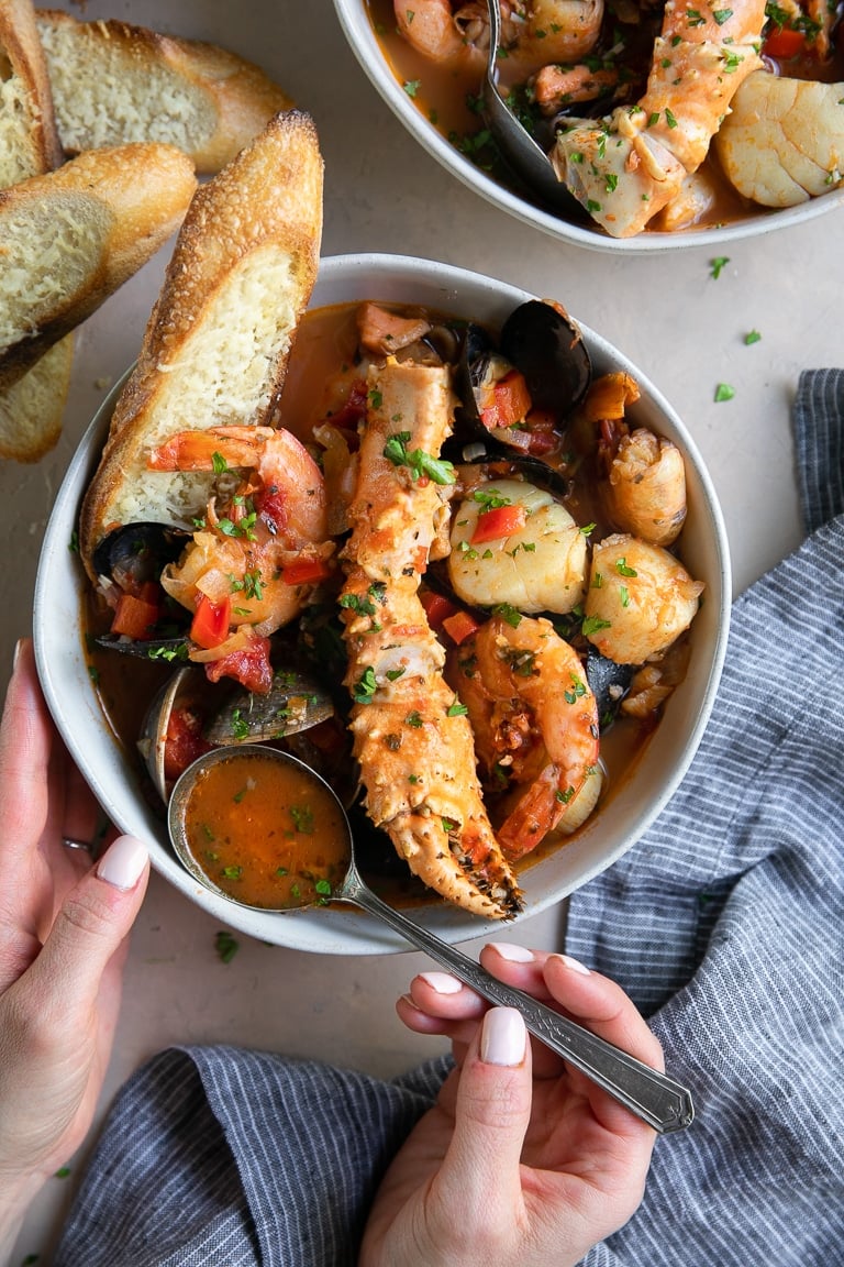 A bowl Cioppino seafood stew filled with shrimp, scallops, crab legs, fish, clams, and mussels and served with slices of bread.