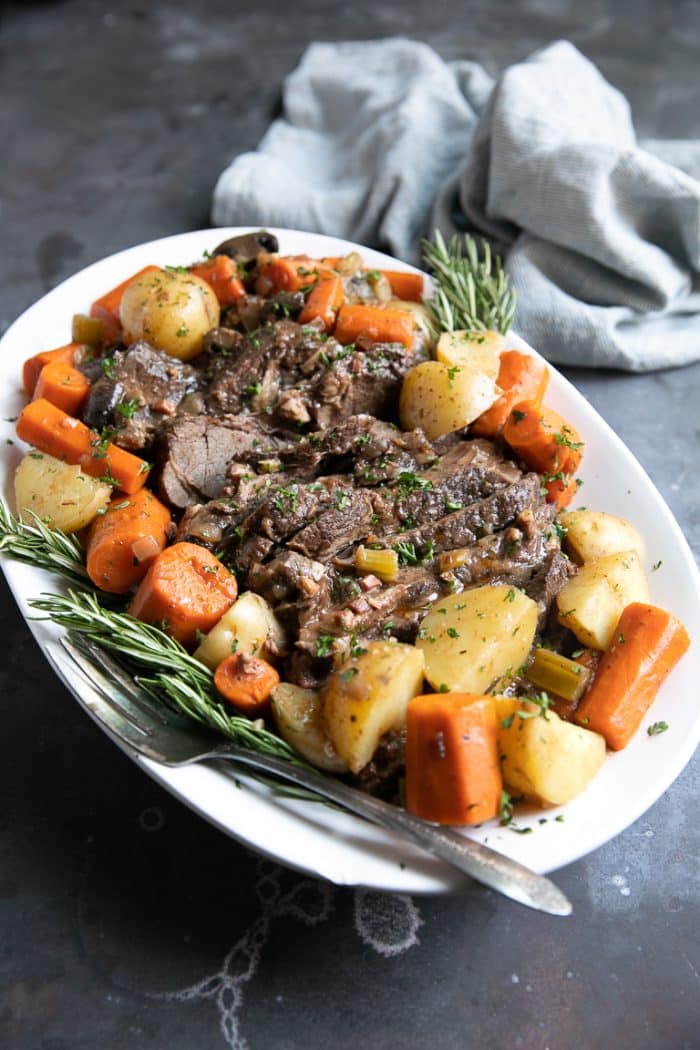 Pot Roast on a white serving tray surrounded with carrots and potatoes.