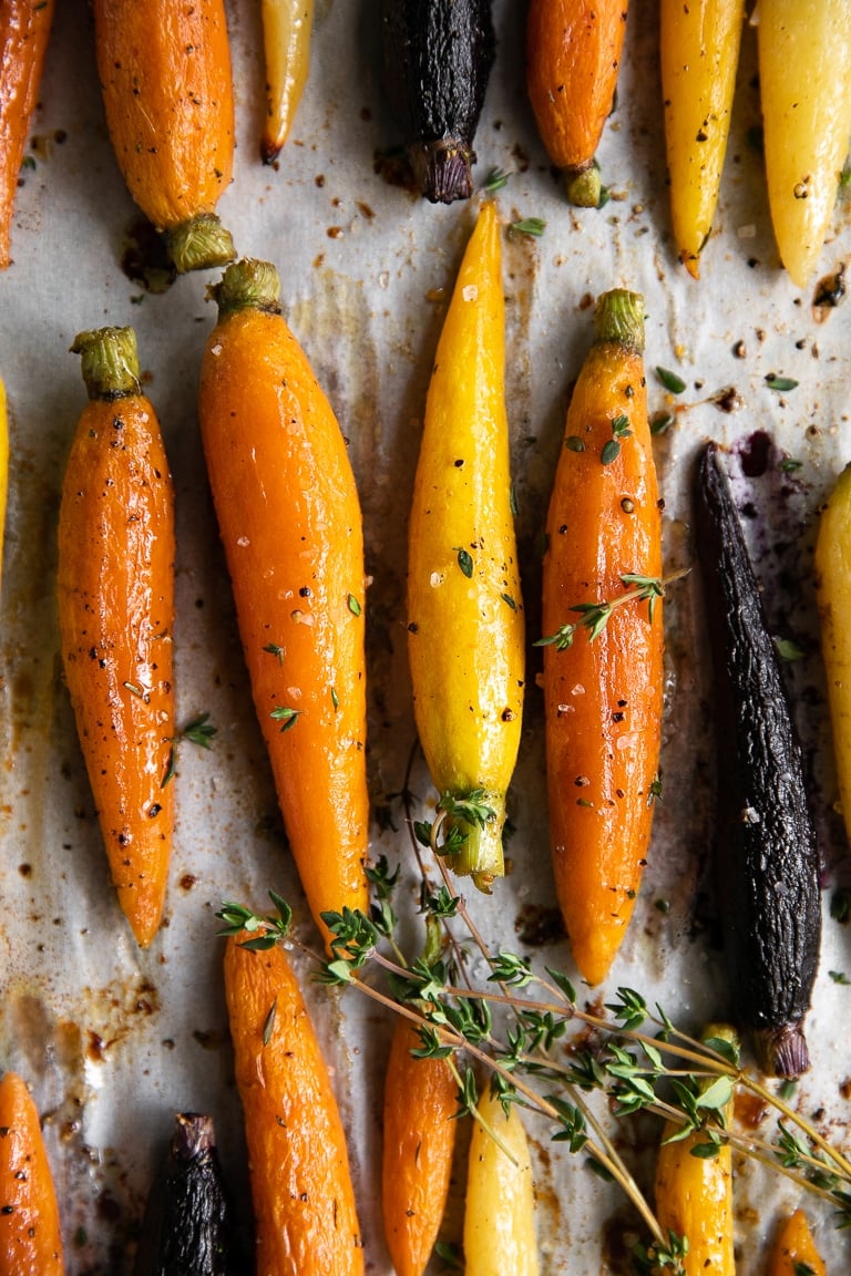Oven-roasted rainbow carrots with caramelized edges, sprinkled with fresh thyme on parchment paper.