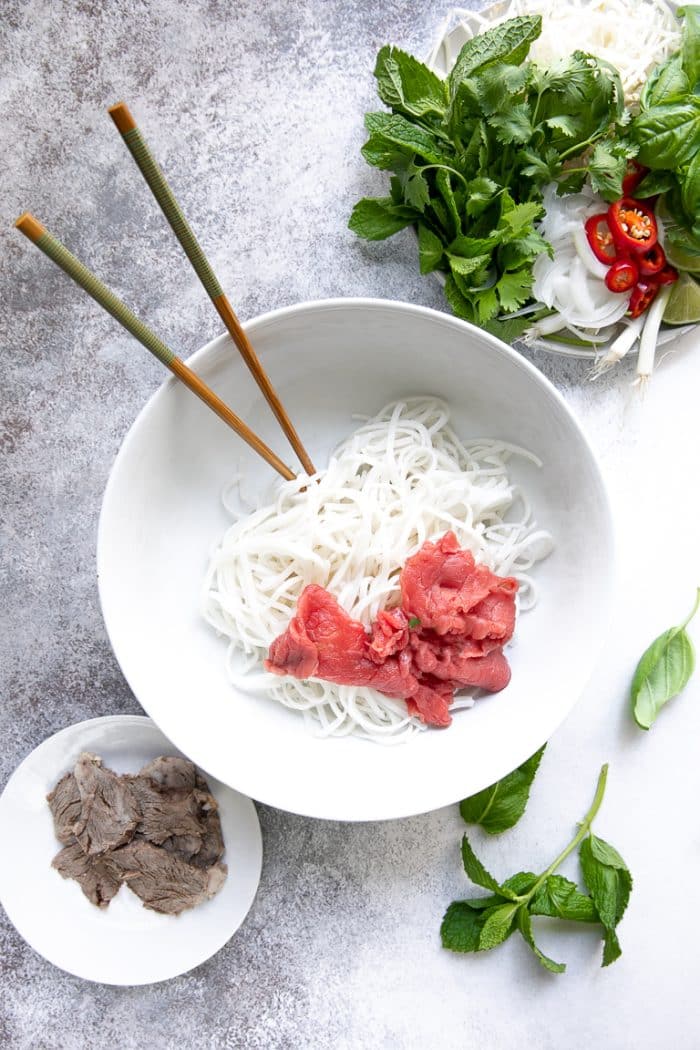 Large white soup bowl filled with rice noodles and thinly sliced beef tenderloin.