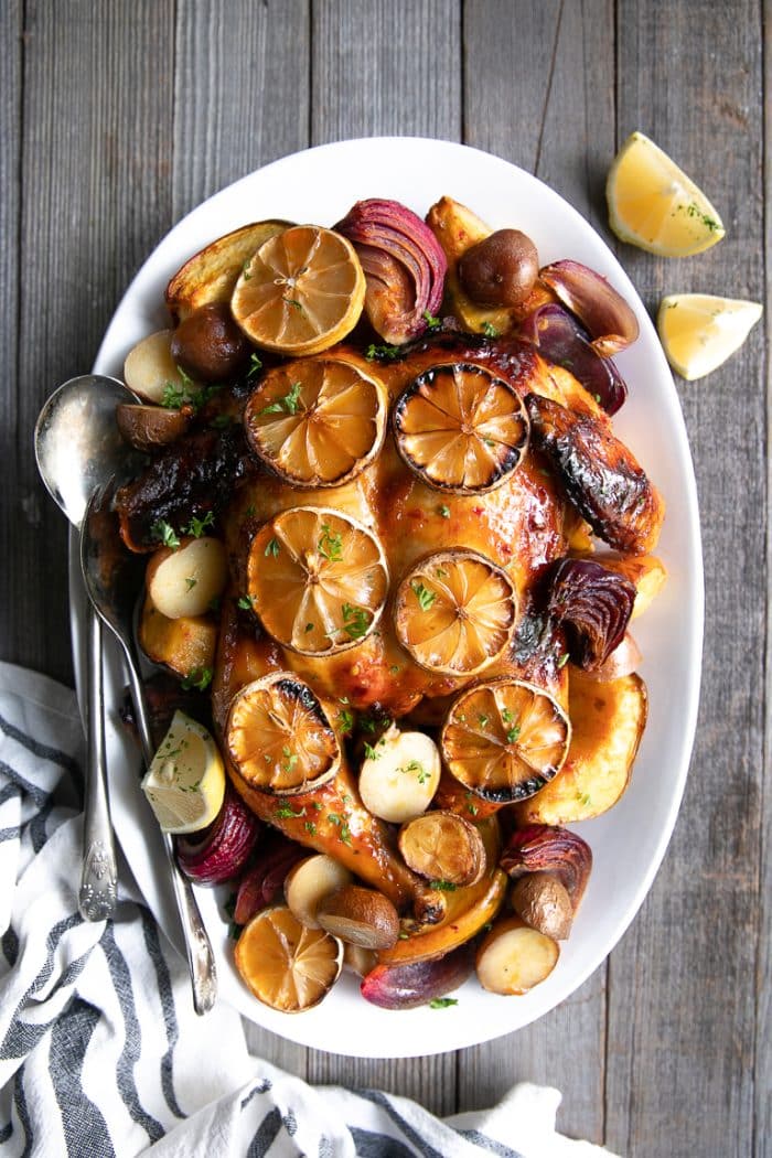 Harissa Chicken on a white platter surrounded by roasted potatoes, onions, and acorn squash and topped with lemons.