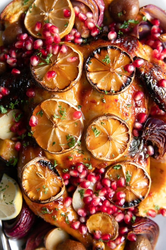 Close-up image of Harissa Chicken topped with sliced lemons and pomegranate arils.