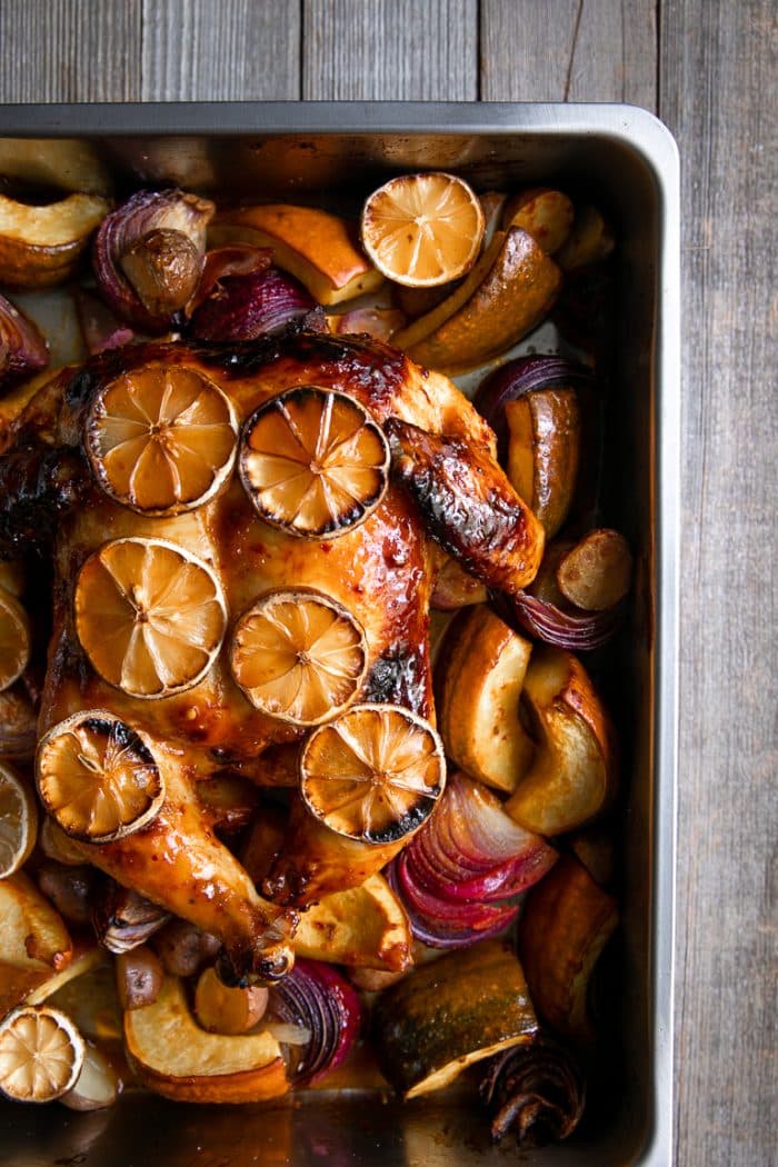 baked harissa chicken in a roasting pan with cooked onions, potatoes, and acorn squash.
