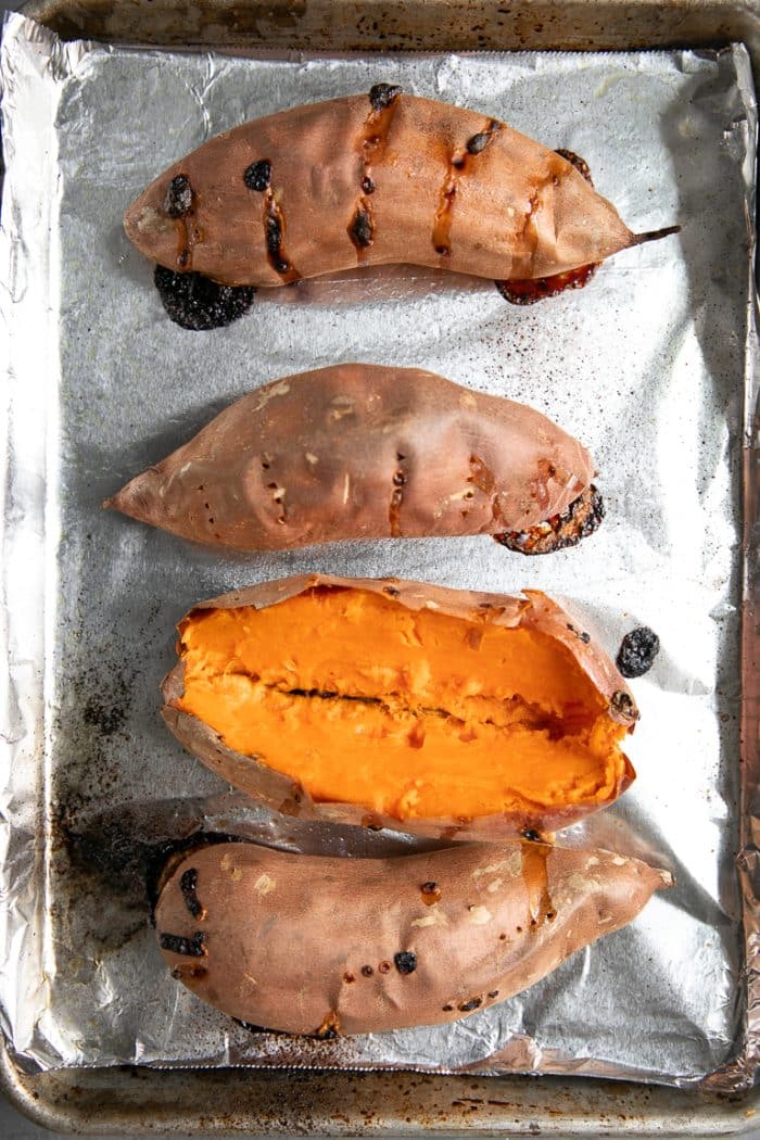 fire bagte søde kartofler på en bageplade med en sød kartoffel skåret ned gennem midten.