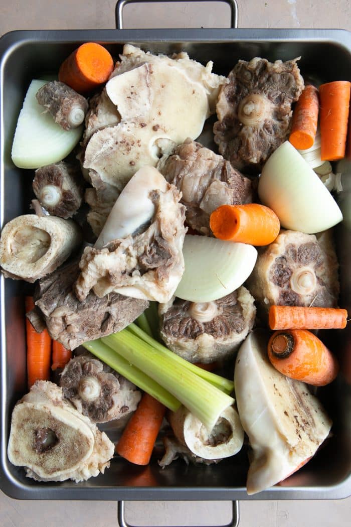 Roasting pan filled with blanched beef bones, carrots, celery, onion, and garlic.