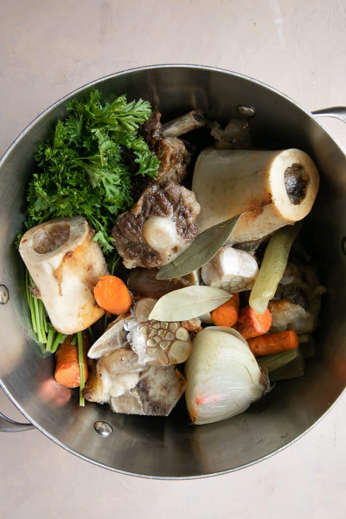 Stockpot filled with roasted beef bones, herbs, and vegetables.