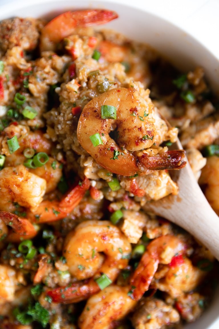 Serving spoon with a large scoop of Jambalaya hovering over a pot filled with jambalaya recipe.