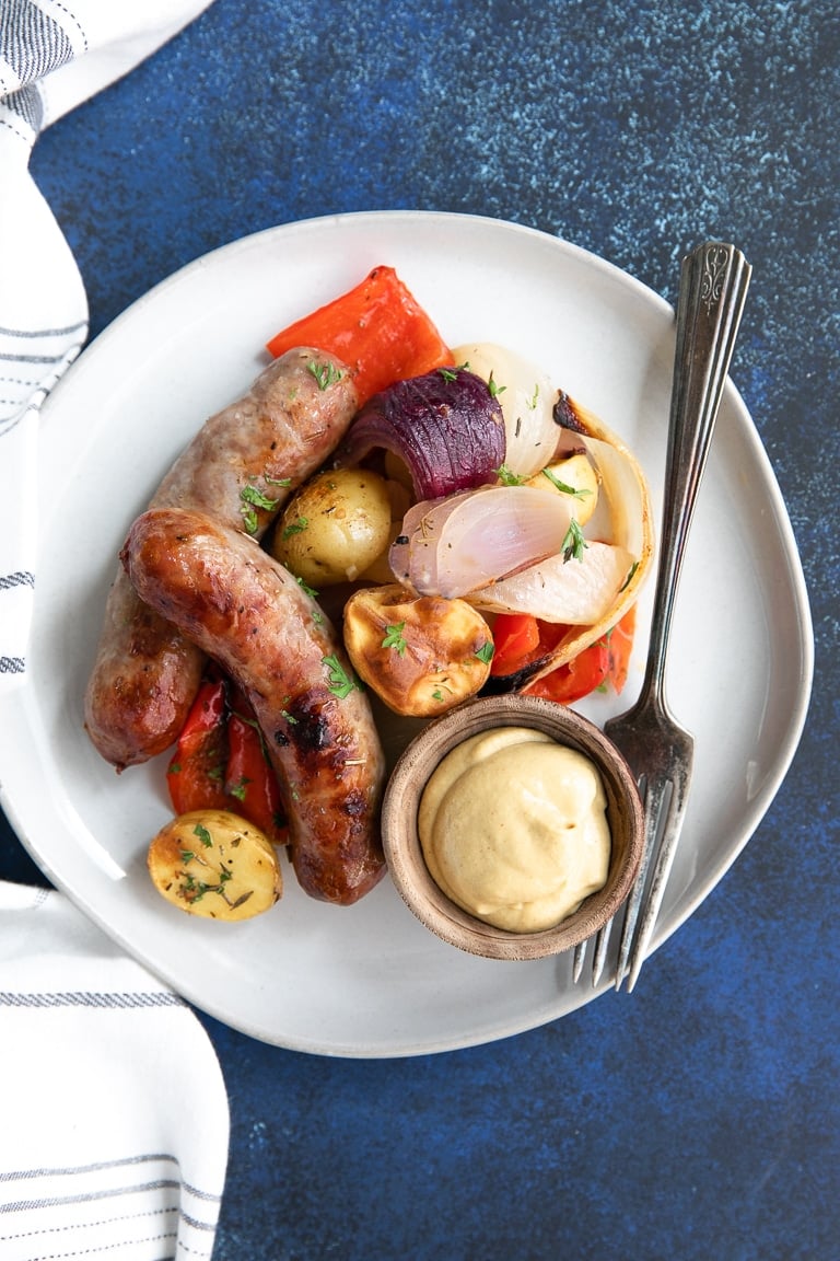 With plate with sausage, potatoes, onions, and bell pepper with a side of mustard.