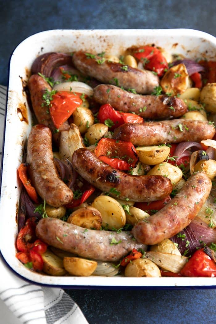 Oven roasted sausage, potatoes, onion, and bell pepper in a white roasting dish.