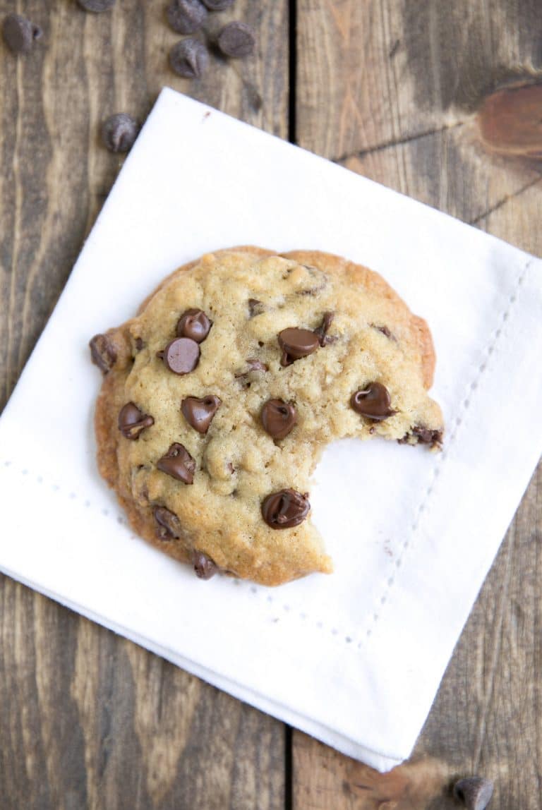 Large brown butter chocolate chip cookie on a white napkin with a bite taken from it.