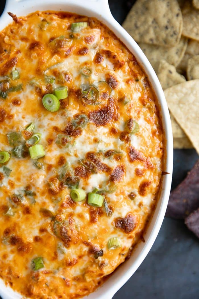 Up-close image of cheesy baked buffalo chicken dip in a white baking dish and topped with green onions