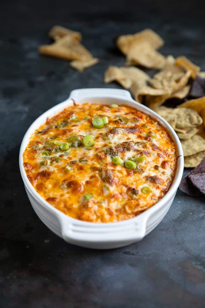 White baking dish filled with cheesy baked dip topped with green onions and served with tortilla chips.