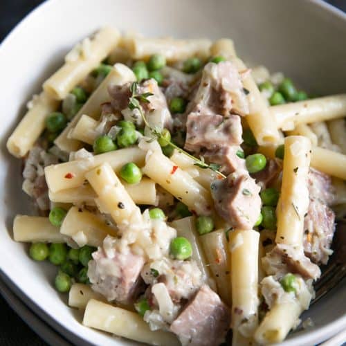 A bowl of food on a plate, with Cream and Ham and pea pasta