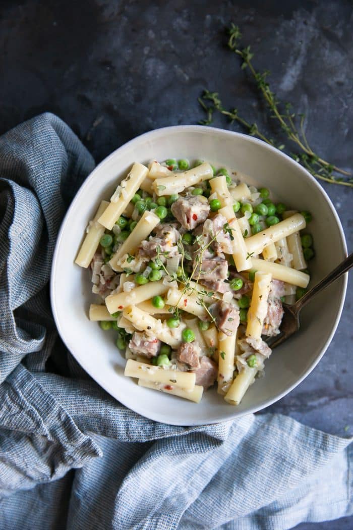 White bowl filled with pasta and covered in a cream sauce with peas and leftover holiday ham.