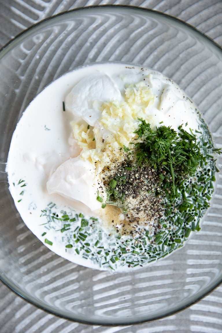 Bowl filled with mayonnaise, milk, Greek yogurt, garlic, dill, chives, and parsley.