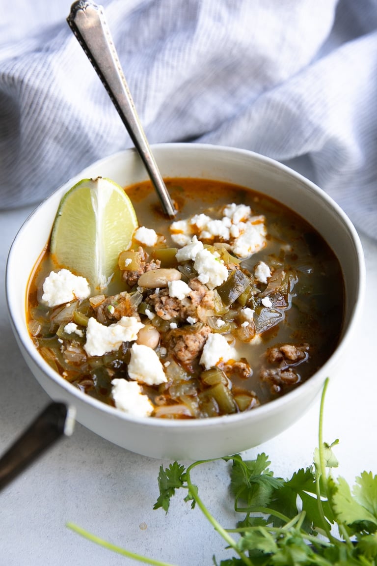 White bowl filled with Pork Green Chile with white beans and garnished with a lime wedge and cotija cheese.