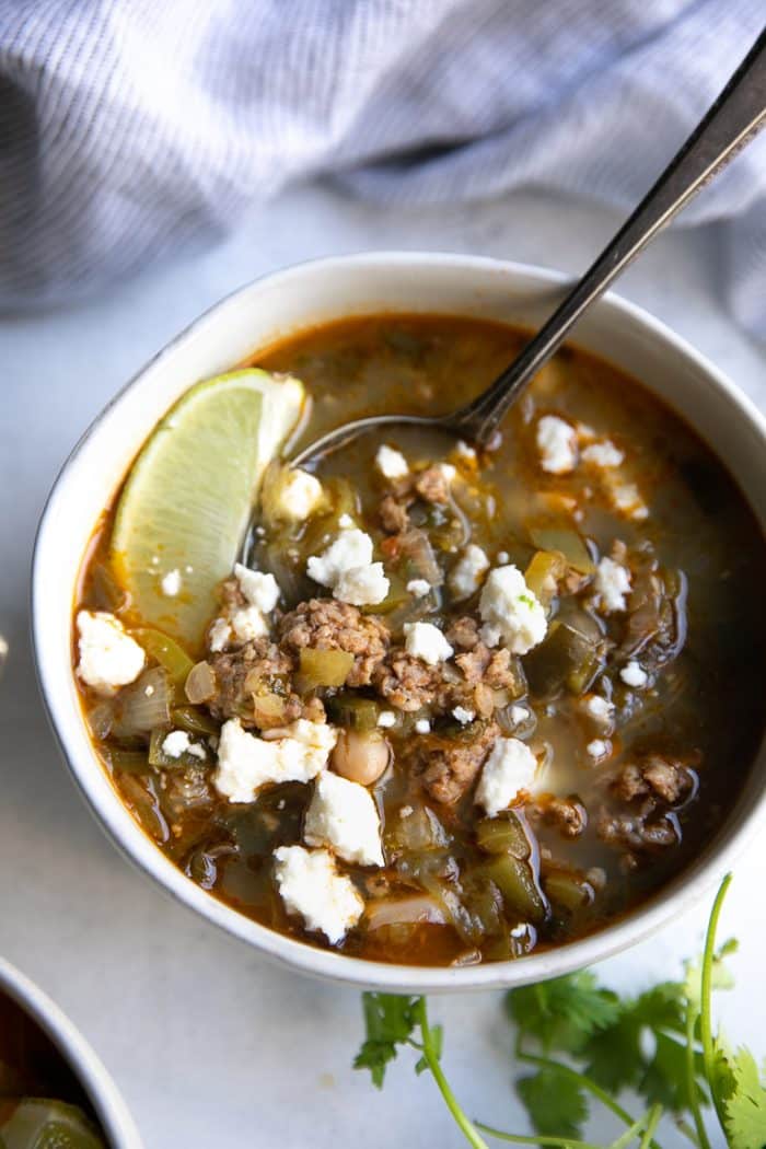 White bowl filled with pork green chili and topped with cotija cheese.