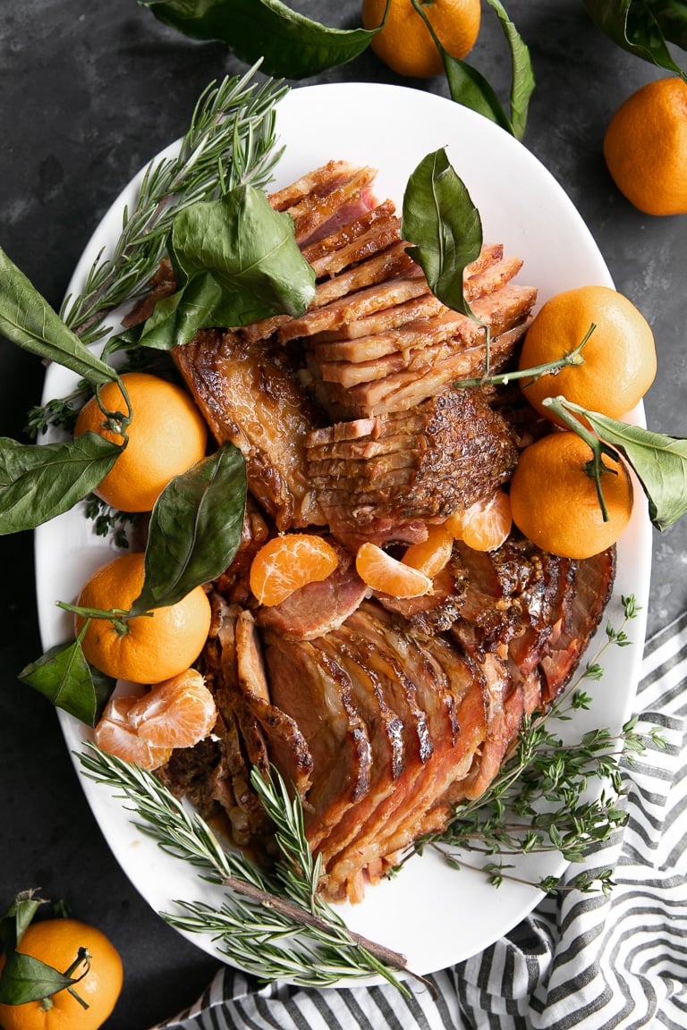 sliced holiday ham on a large white serving plate with mandarins 