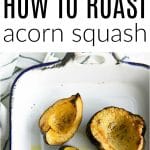 Roasted acorn squash halves in a white enamel baking dish, golden brown and seasoned with salt and pepper, ready to serve.
