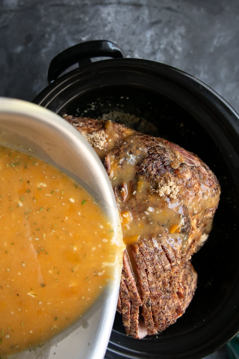 pouring apricot marmalade glaze onto slow cooker ham.