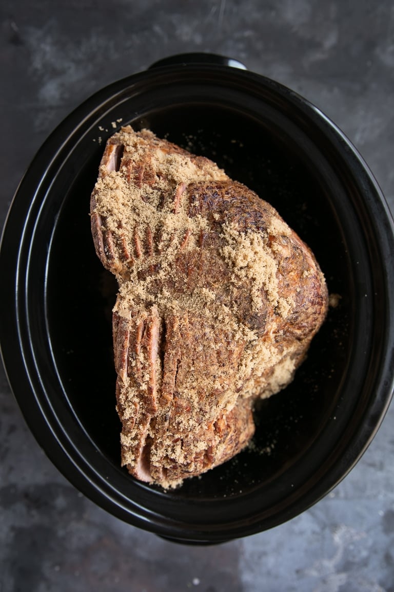 uncooked ham in a slow cooker covered in brown sugar.