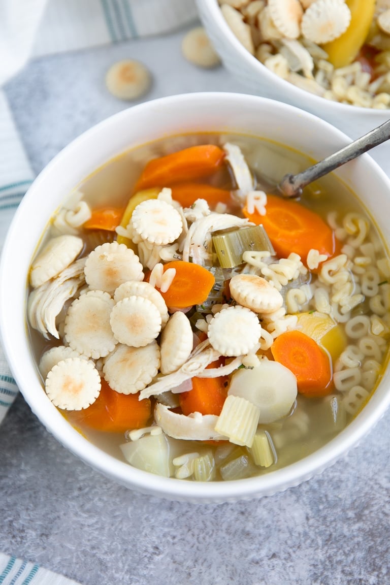 White bowl filled with with chicken alphabet soup with orange, yellow, and white carrots.