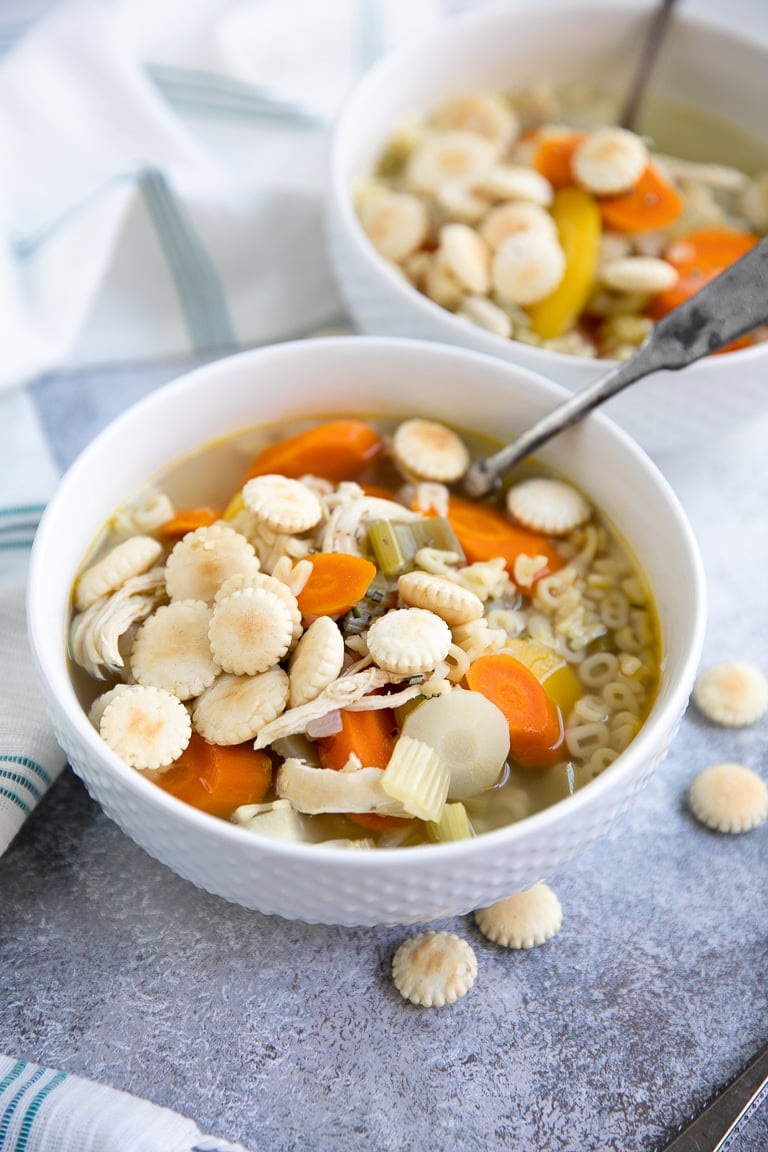 Side view of alphabet soup with celery, and multi-colored carrots, topped with oyster crackers.
