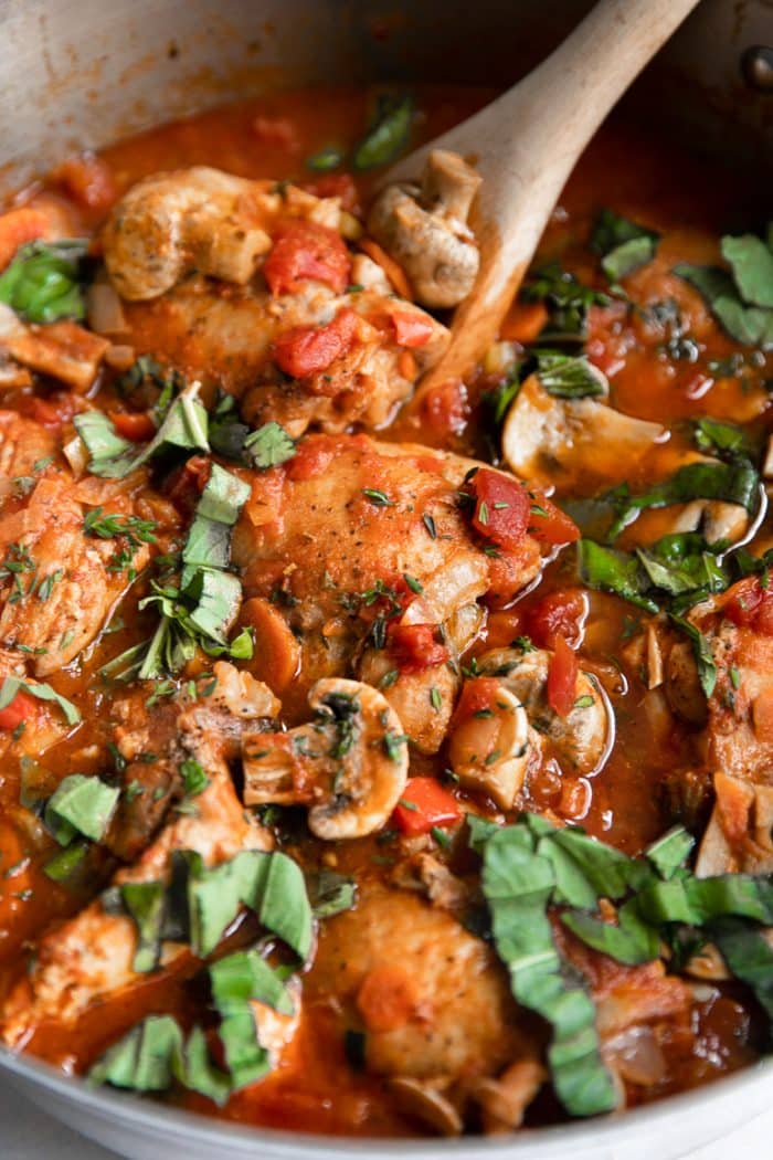 Large shallow pot filled with skinless bone-in chicken thighs cooked with tomatoes and mushrooms in a tomato sauce.