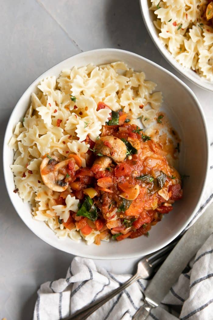 Chicken cacciatore served with pasta noodles in a wide shallow white bowl.