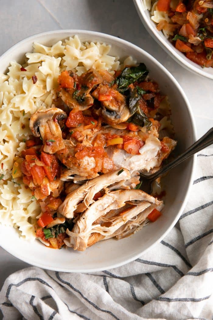 White bowl filled with buttered noodles and fall off the bone chicken cacciatore.