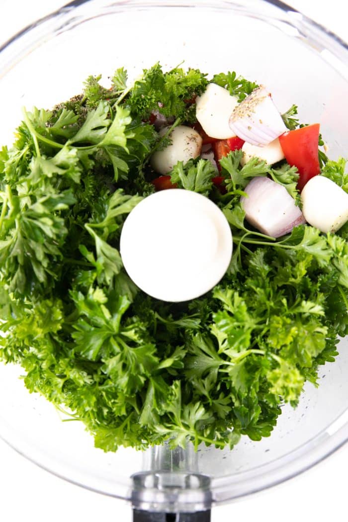 A blender with parsley, garlic, red wine vinegar, oregano, garlic, and a red chili for homemade Chimichurri.