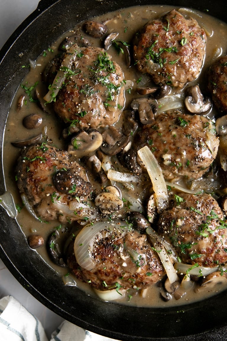 Salisbury steak meat patties with mushroom and onions in a rich gravy in a cast iron skillet.