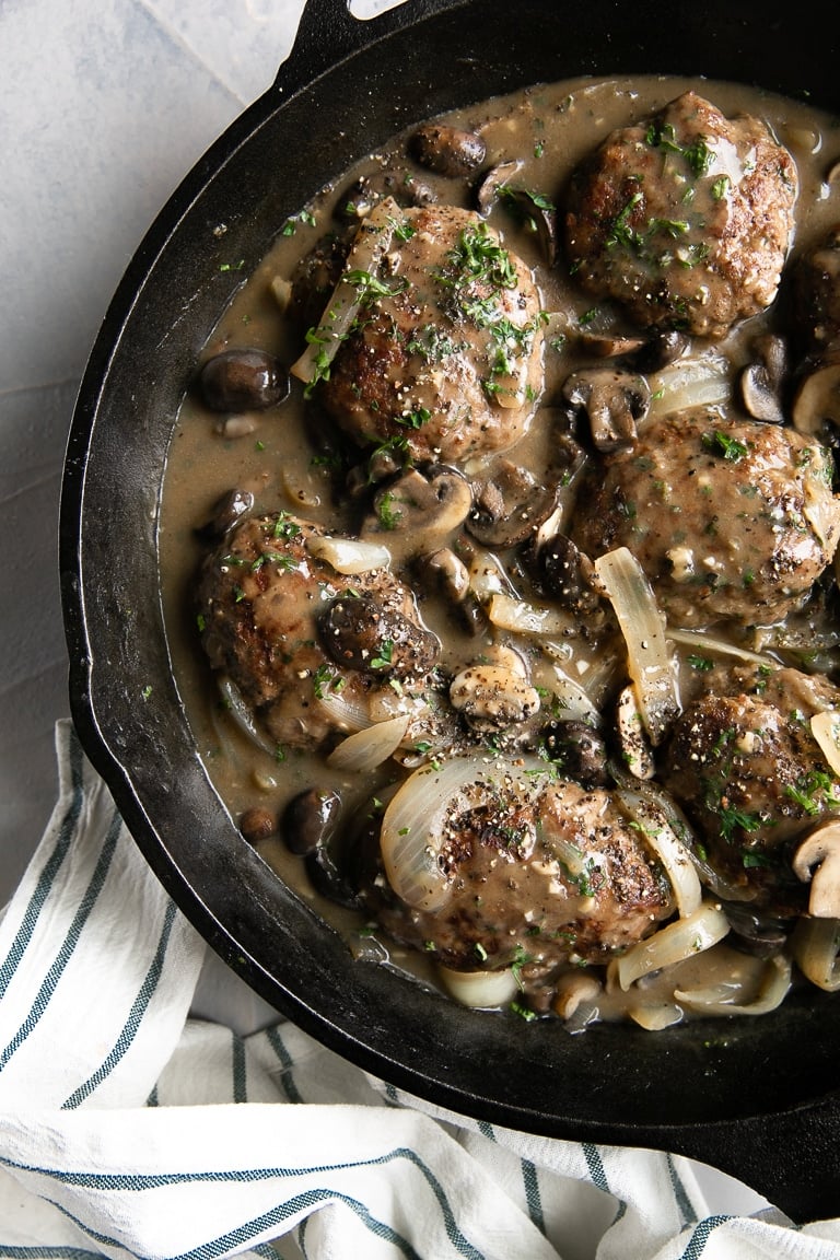 Salisbury steak meat patties with mushroom and onions in a rich gravy in a cast iron skillet.