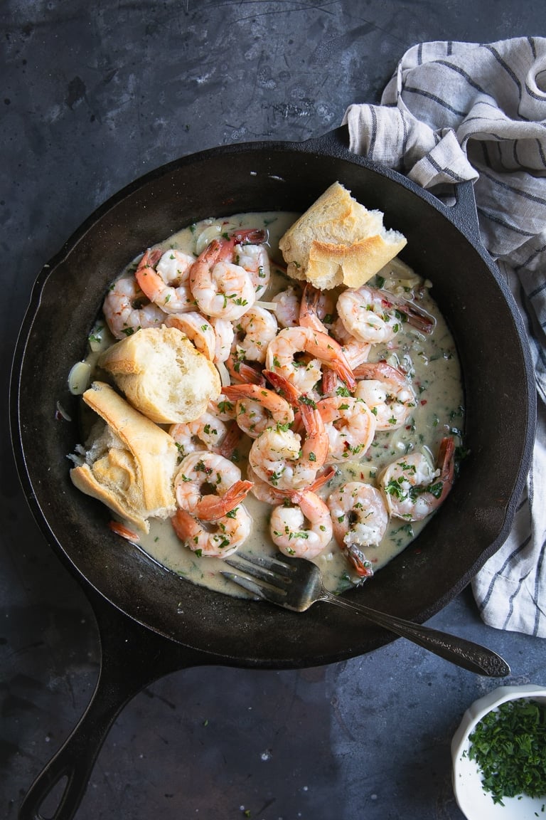 Cast iron skillet filled with large shrimp cooked in a garlic butter sauce and served with fresh bread.