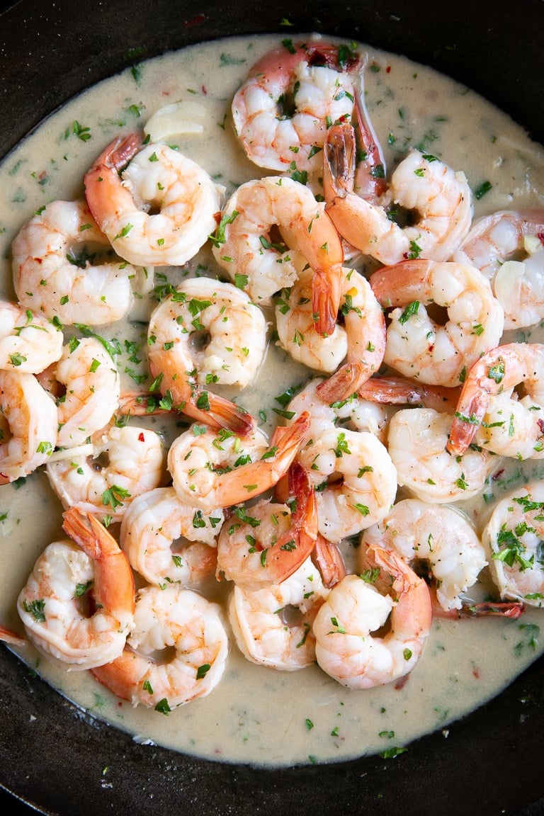 Black cast iron skillet filled with shrimp scampi and garnished with fresh parsley