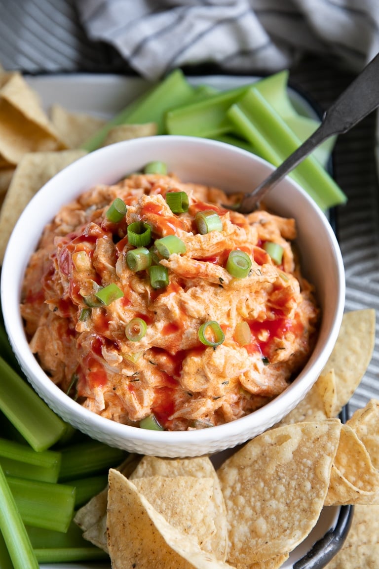 White Bowl filled with Slow Cooker Buffalo Chicken Dip and garnished with chopped green onion.