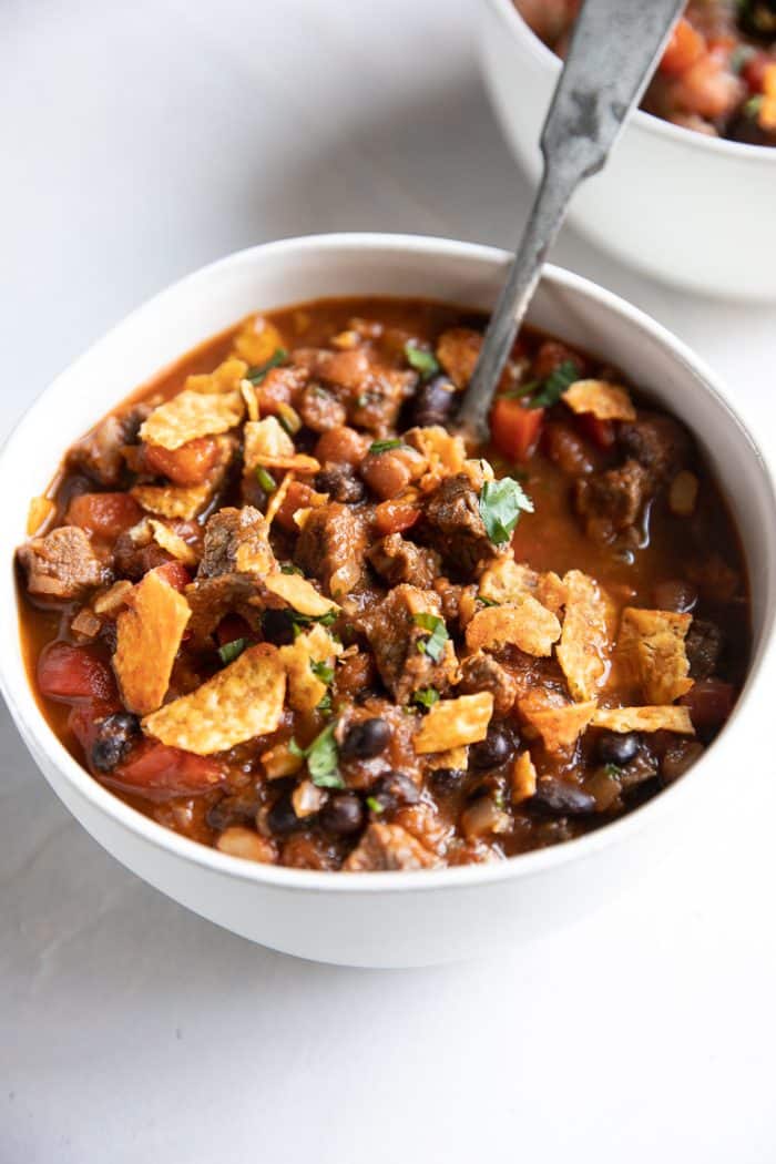 White bowl filled with steak and black bean chili and topped with nacho doritos