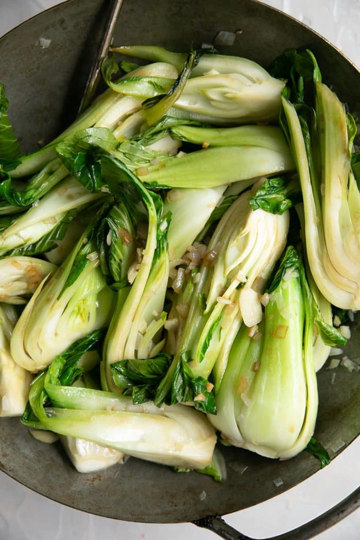 Baby bok choy being cooked in a wok with garlic and shallots.