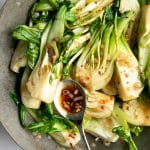 Bok Choy being cooked in a wok with a spoonful of garlic sauce