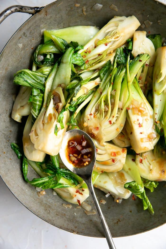 Sauteed baby bok choy fully cooked in an old heavy wok sprinkled with crushed red chili flakes.