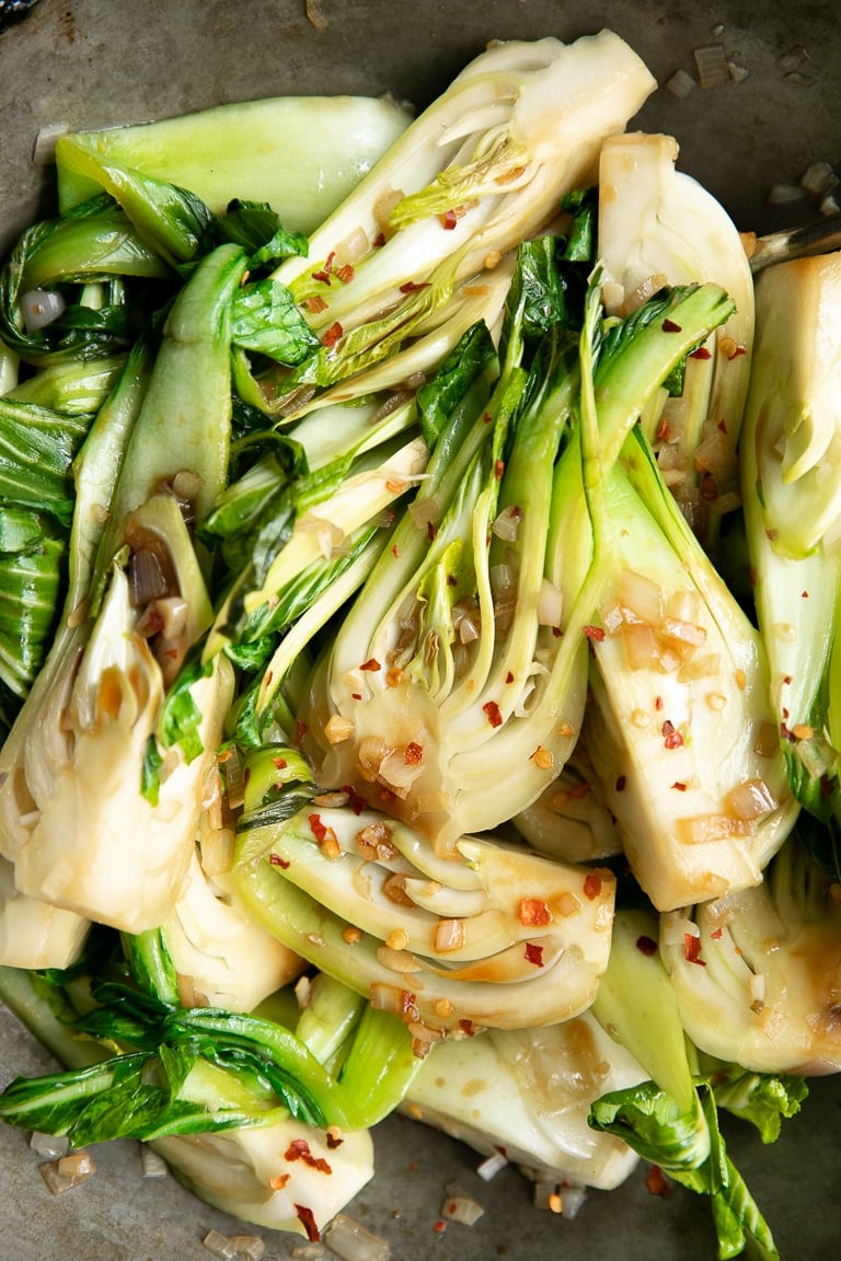 Stir-fried Garlic baby bok choy in a wok with shallots and soy sauce.