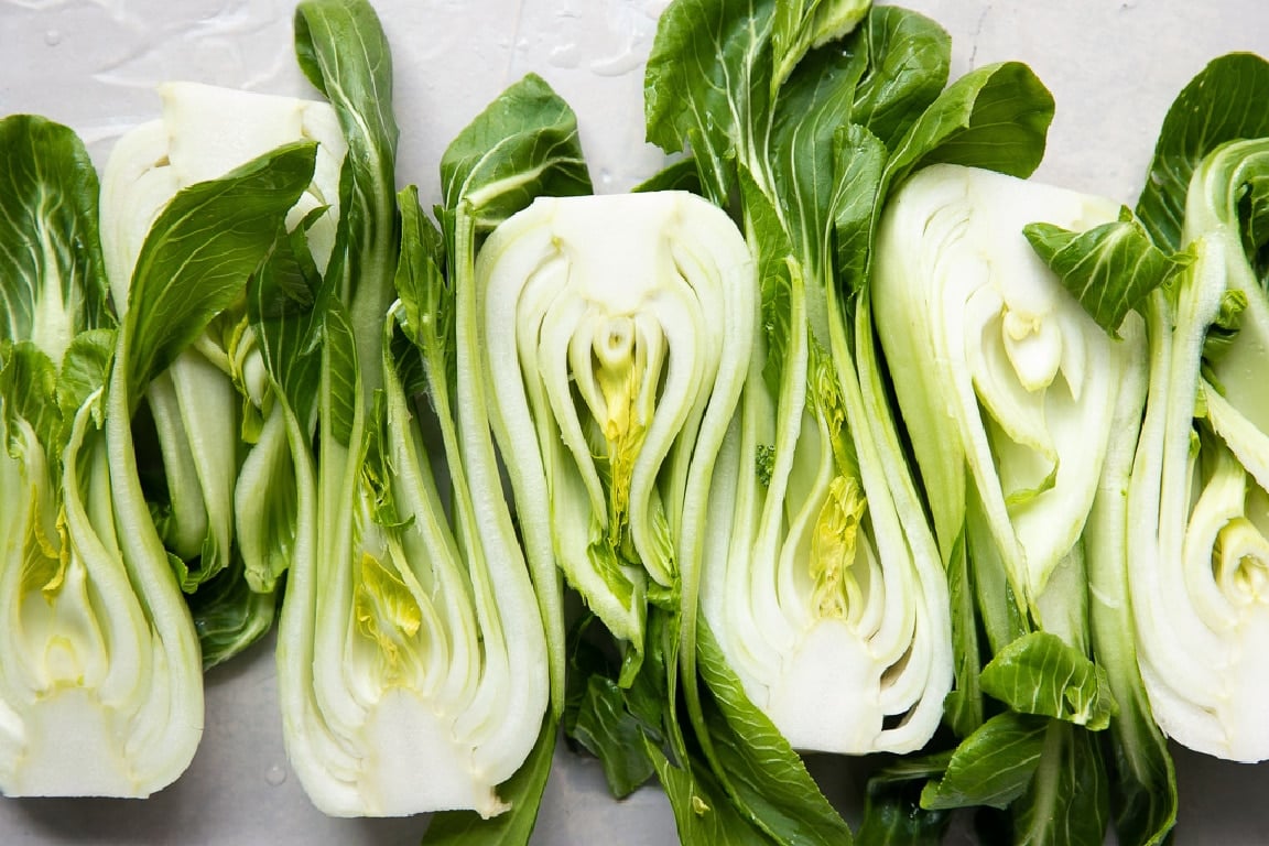 Raw baby bok choy cut in half lengthwise, lined up on a white surface