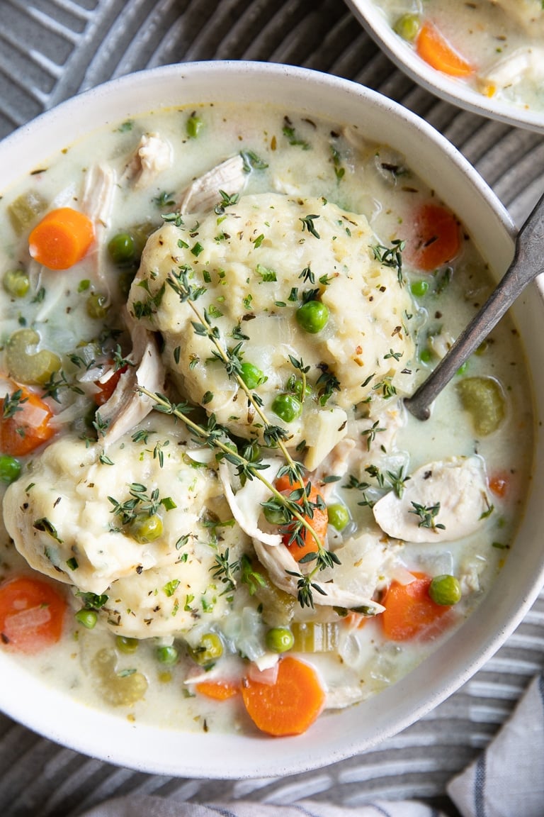 A white bowl filled with homemade chicken dumplings garnished with fresh thyme.