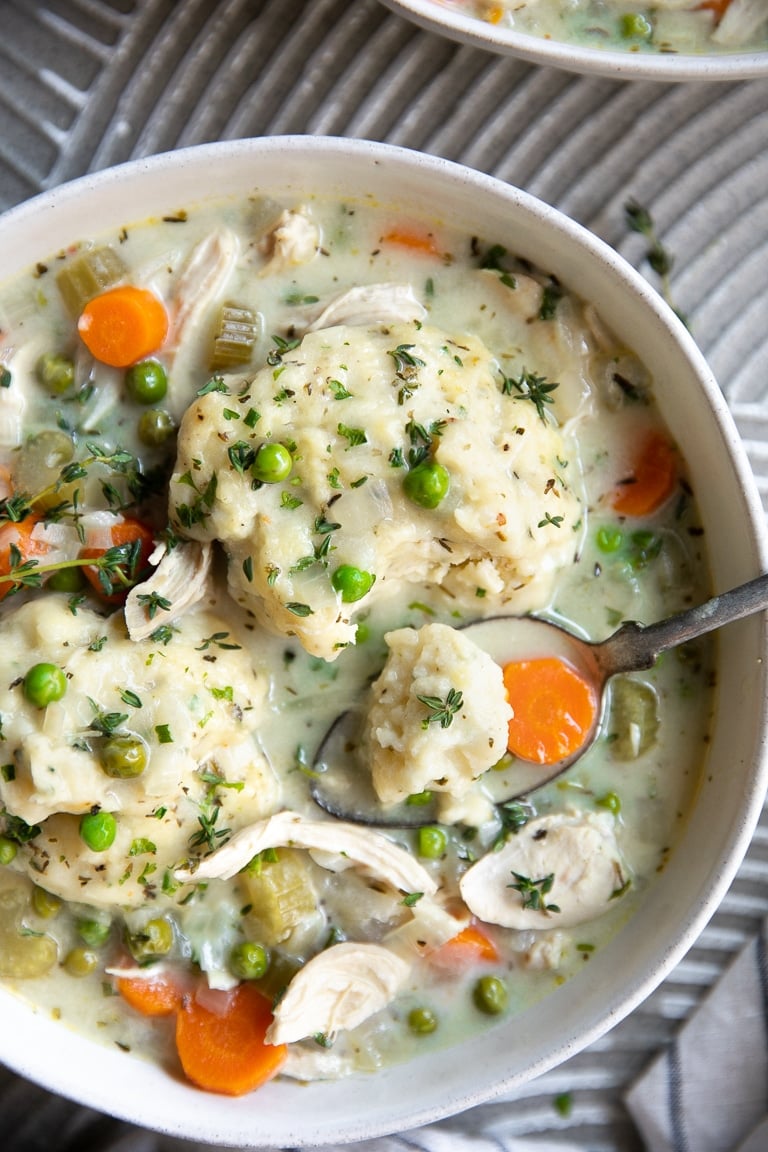 A white bowl filled with homemade chicken dumplings garnished with fresh thyme.