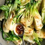 Stir-fried garlic bok choy in a large wok with diced shallots.