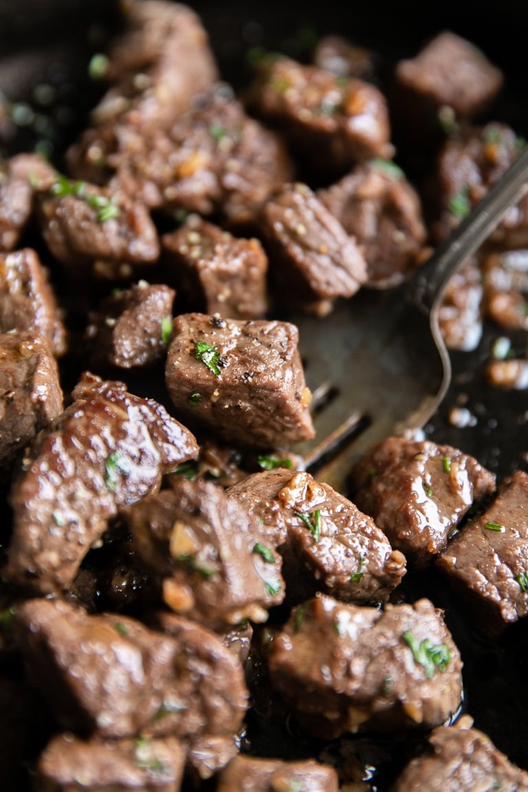 Close up image of cut-up sirloin steak bites cooked in a garlic butter sauce.