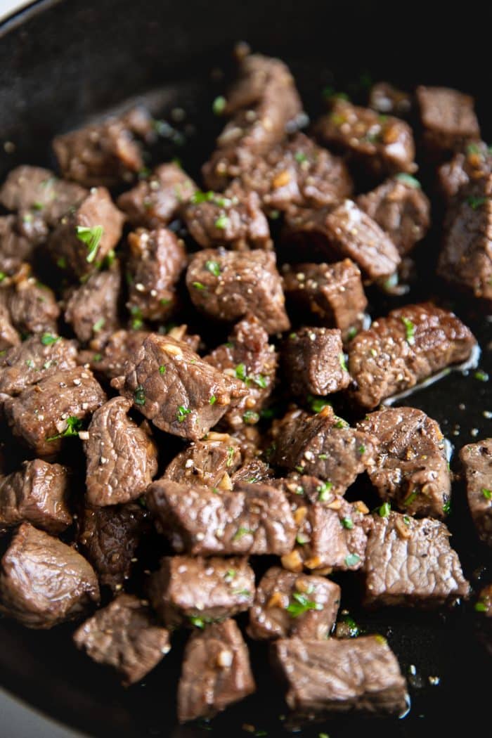 Steak bites cooked in garlic and butter in a cast iron skillet.
