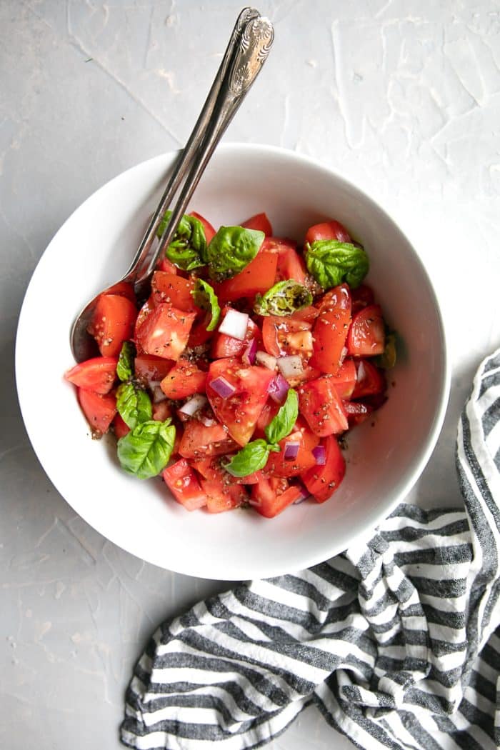 Fresh Tomato Basil Salad tossed in olive oil and balsamic vinegar and served in a large white salad bowl.