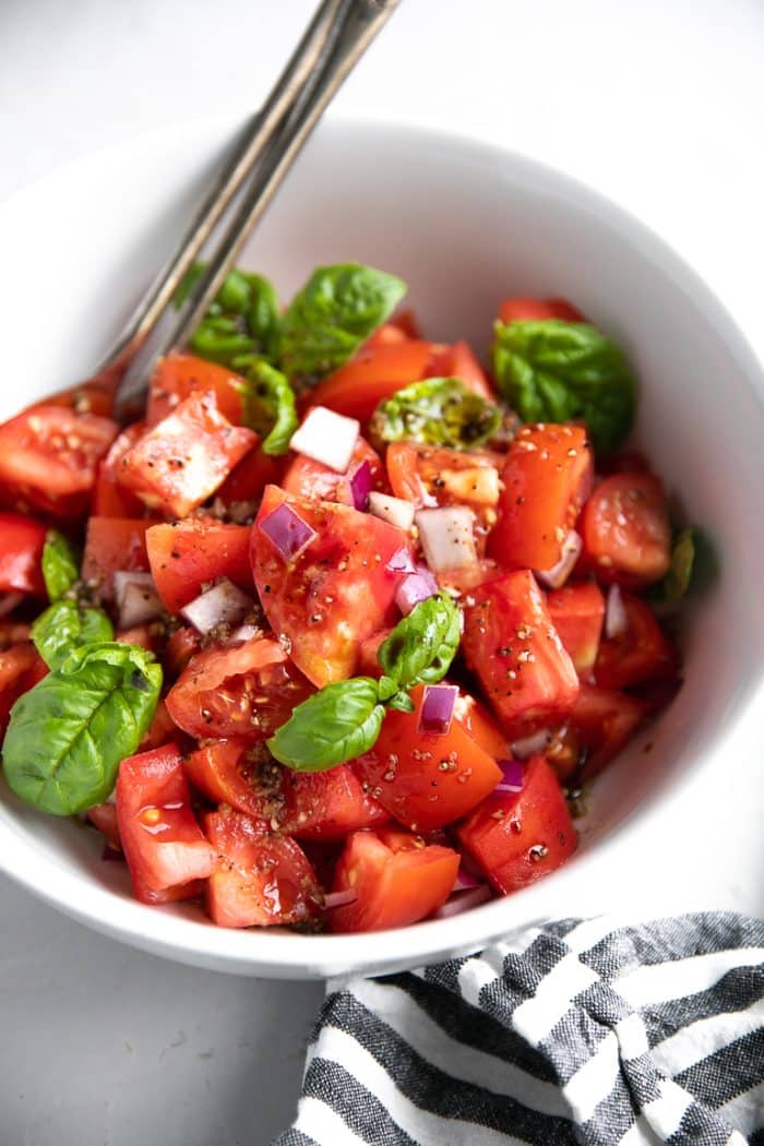 Chopped tomatoes, red onion, and basil in a white bowl tossed with balsamic vinegar and olive oil.